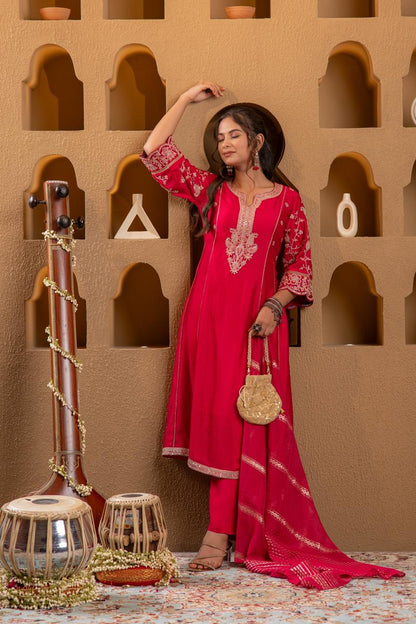 Artistic pose of rani pink Viscose Silk kurta set with gold floral embroidery and zari dupatta, sitar backdrop - Jagranee