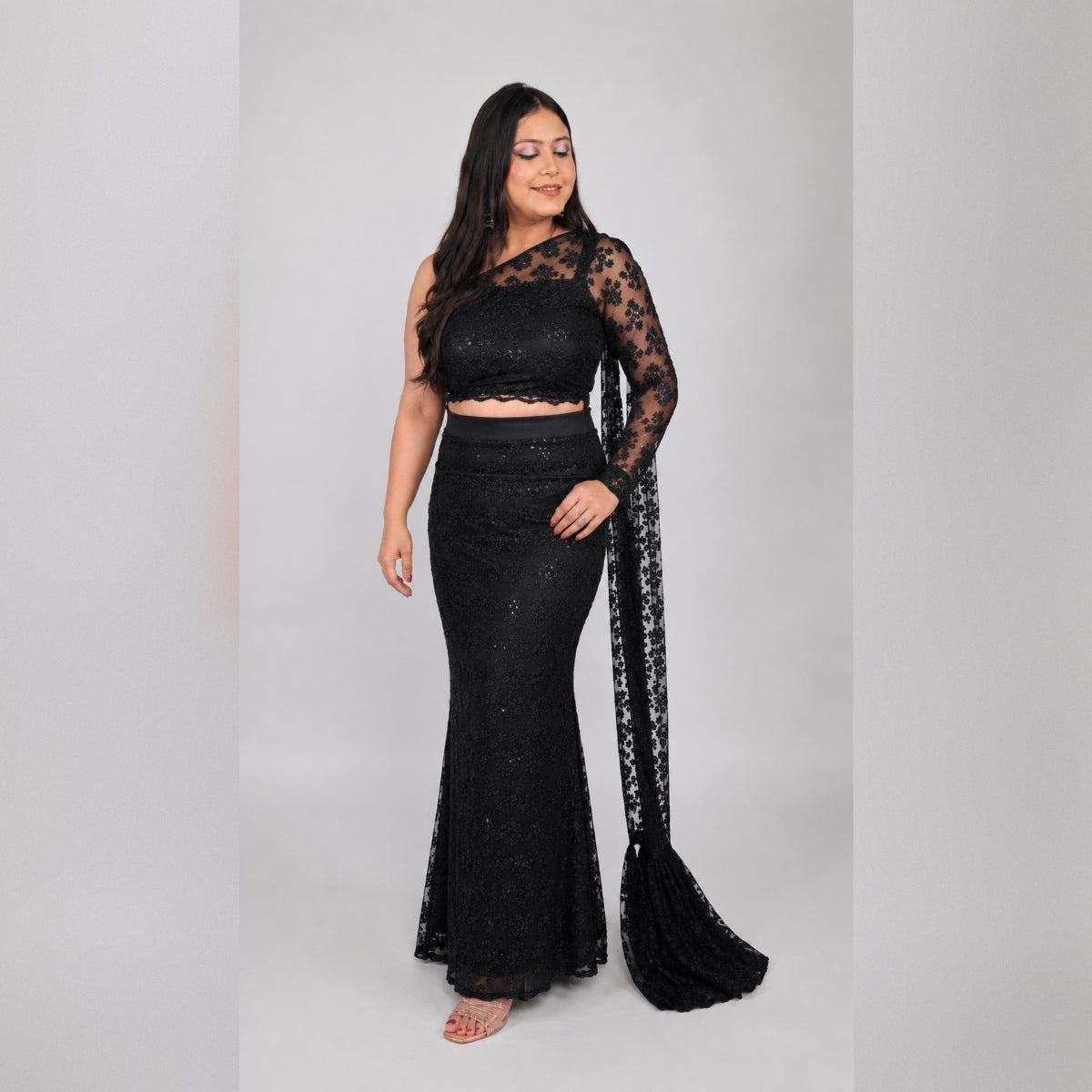 Front view of black sequin net one-shoulder mermaid saree gown set with sheer lace sleeve and pallu trail flowing - Jagranee