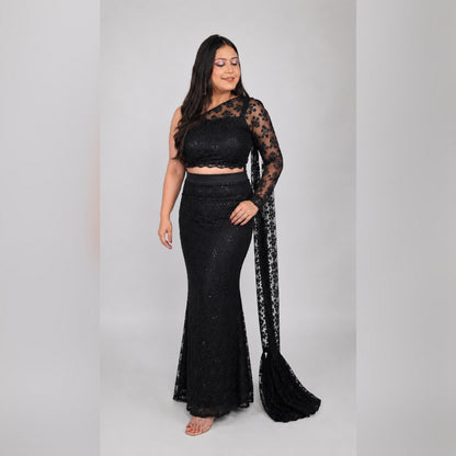 Front view of black sequin net one-shoulder mermaid saree gown set with sheer lace sleeve and pallu trail flowing - Jagranee