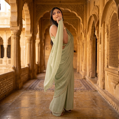 Sage green satin crepe saree with pearl-edged pallu draped over sleeveless blouse in Jaisalmer haveli courtyard - Jagranee