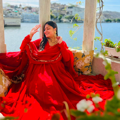 Woman seated in lakeside palace gazebo wearing red flowing georgette Anarkali gown with gold lace dupatta, Udaipur lake view - Jagranee