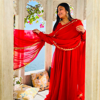 Woman standing in white marble palace holding flowing red georgette dupatta with gold lace border, lake visible through arches - Jagranee