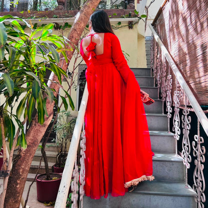 Back view of red georgette Anarkali gown showing tie-back bow detail and gold lace hemline on heritage haveli staircase - Jagranee